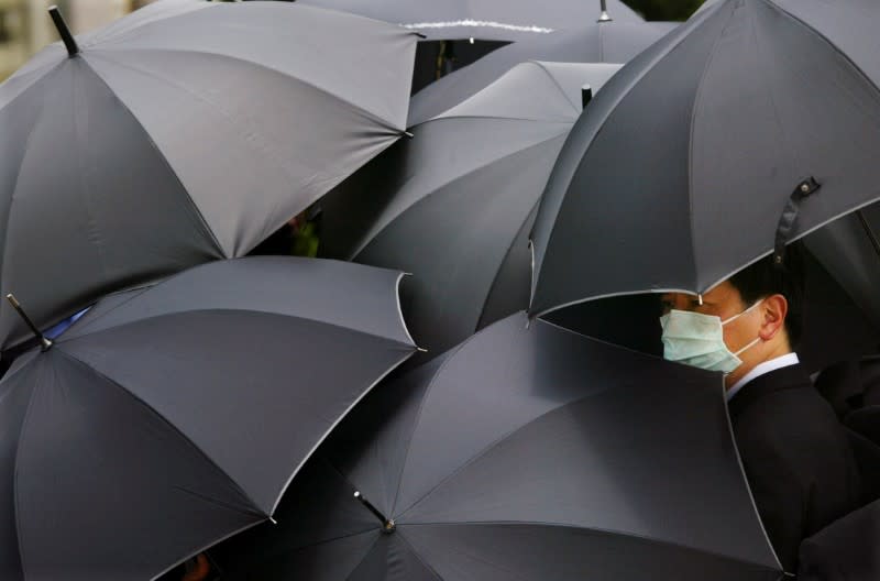 FILE PHOTO: A mourner wearing a mask to protect himself from SARS stands under an umbrella during the funeral of SARS doctor Tse Yuen-man in Hong Kong