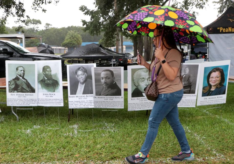 A woman with an umbrella walks past portraits of historical black leaders at Juneteenth festivities in Daytona Beach.