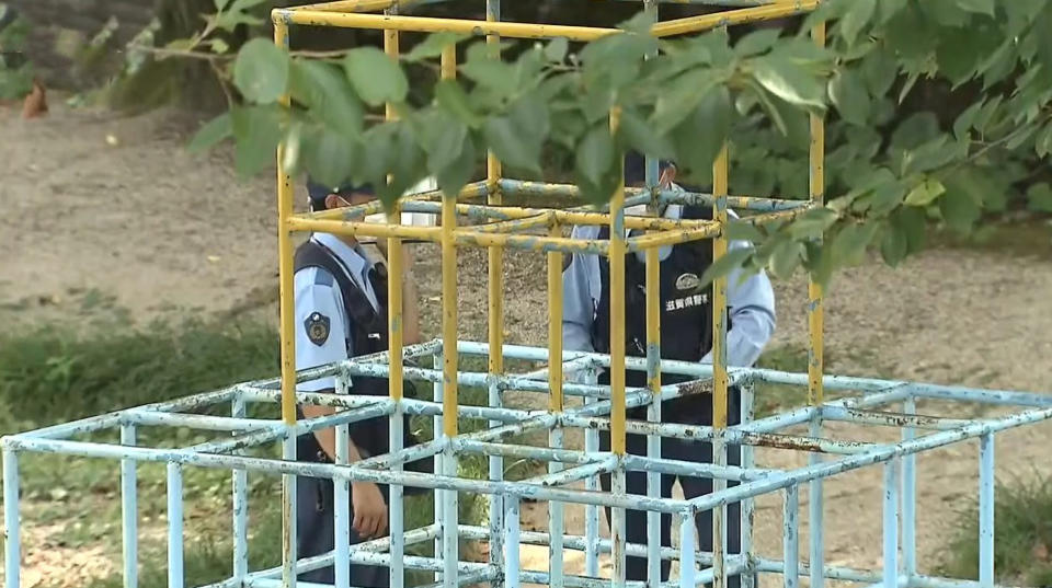 Two police officers stand next to a jungle gym in Japan where a little girl was found after she was allegedly killed by her brother.