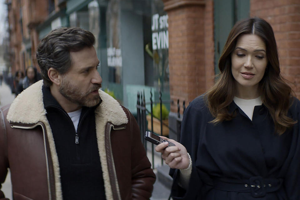 two people walking outside while one holds out a recorder