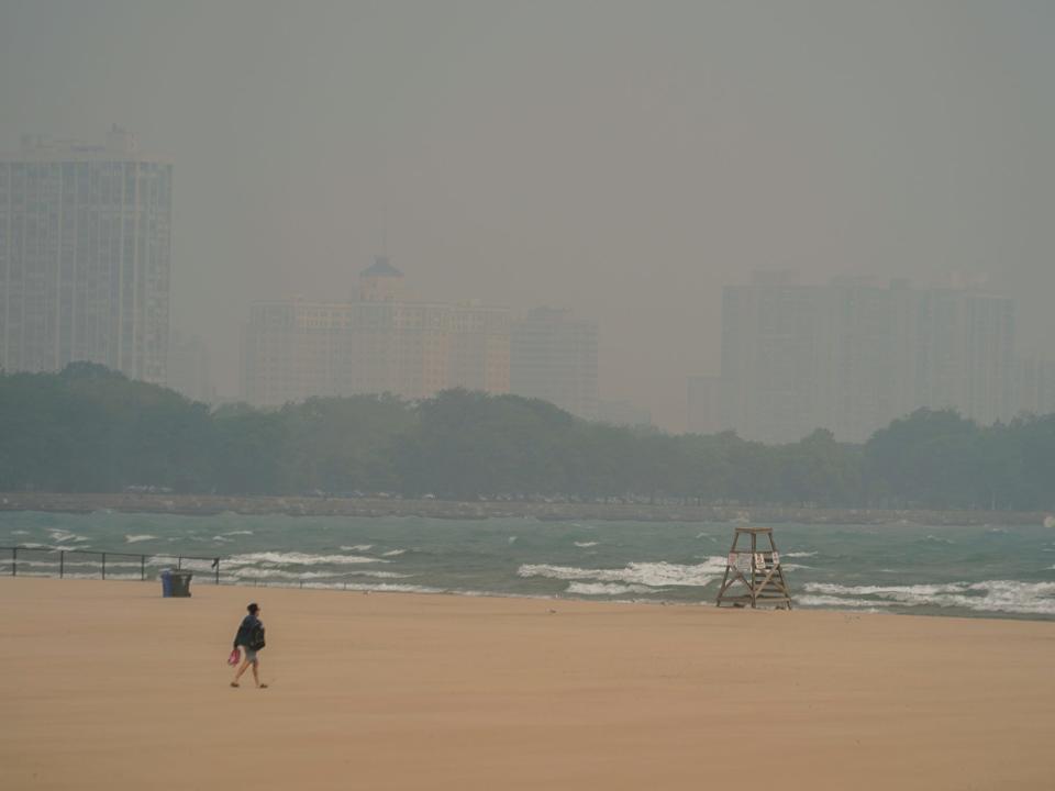 A person walks on Montrose Beach as buildings behind the shore are blanketed in haze from Canadian wildfires Tuesday, June 27, 2023, in Chicago.