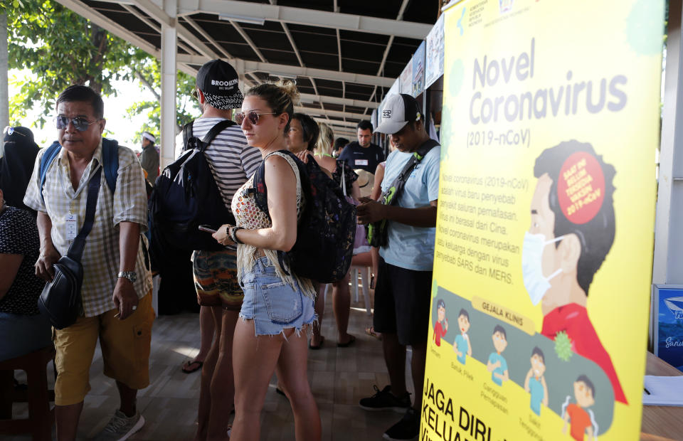 Photo shows foreign tourists standing near an information banner on the coronavirus at a harbour as they wait for their departure in Bali, Indonesia.