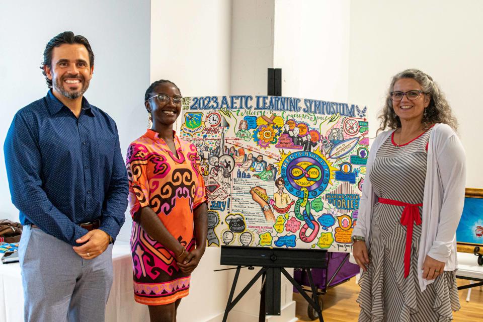 Graphic illustrator Tiiwon Siaway (center) displays her work at the Air Education and Training Command Learning Symposium, Aug. 24, 2023. Standing with Siaway are Marcus Carrion (left), AETC symposium facilitator and co-chair, and Dr. Wendy Walsh (right), AETC chief learning officer.