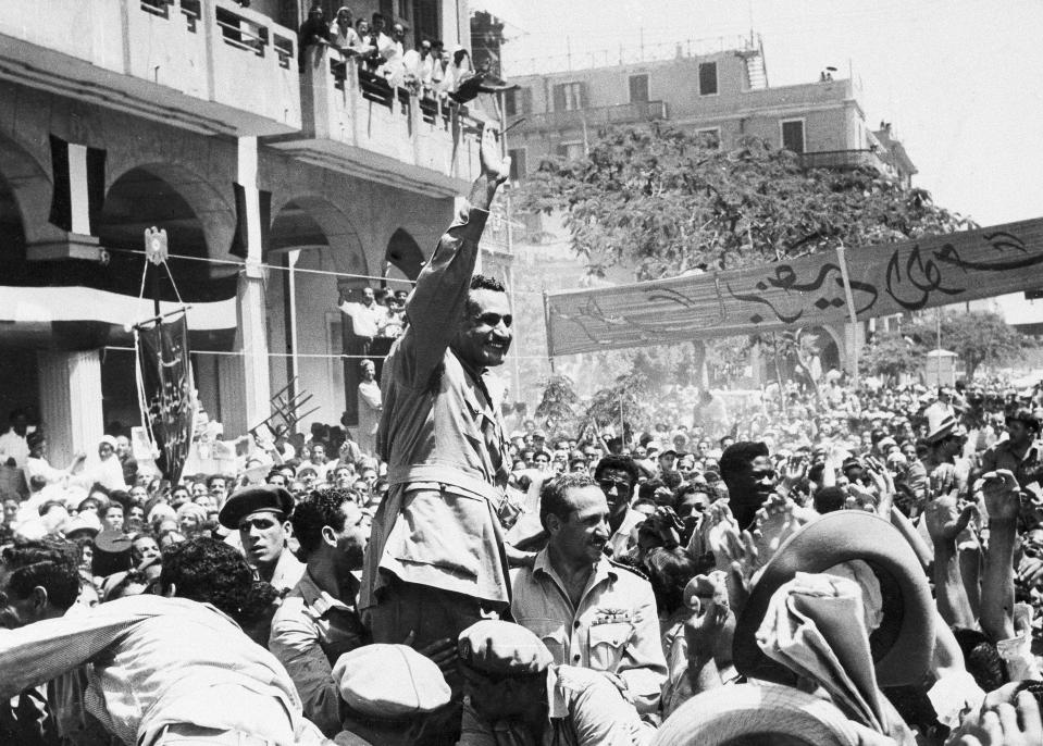 FILE - In this June 18, 1956 file photo, Egyptian leader Gamal Abdel Nasser waves as he moves through Port Said, Egypt, during a ceremony in which Egypt formally took over control of the Suez Canal from Britain. Since it opened in 1869, the canal has been a source of national pride and a focus of international conflict. Now, a skyscraper-sized container ship called the Ever Given got stuck sideways across the waterway since Tuesday, March 23, 2021 . The obstruction has halted canal traffic, valued at over $9 billion a day. (AP Photo, File)