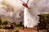 A firefighting helicopter drops water to extinguish flames during a wildfire at the village of Kineta, near Athens, on July 24