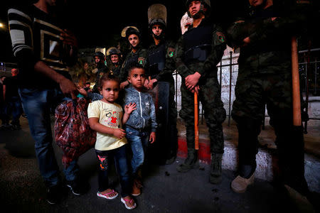 Children walk as members of Palestinian security forces stand guard during a protest calling on President Mahmoud Abbas to end financial sanctions on Palestinians in Gaza, in Ramallah, in the occupied West Bank, June 13, 2018. REUTERS/Mohamad Torokman