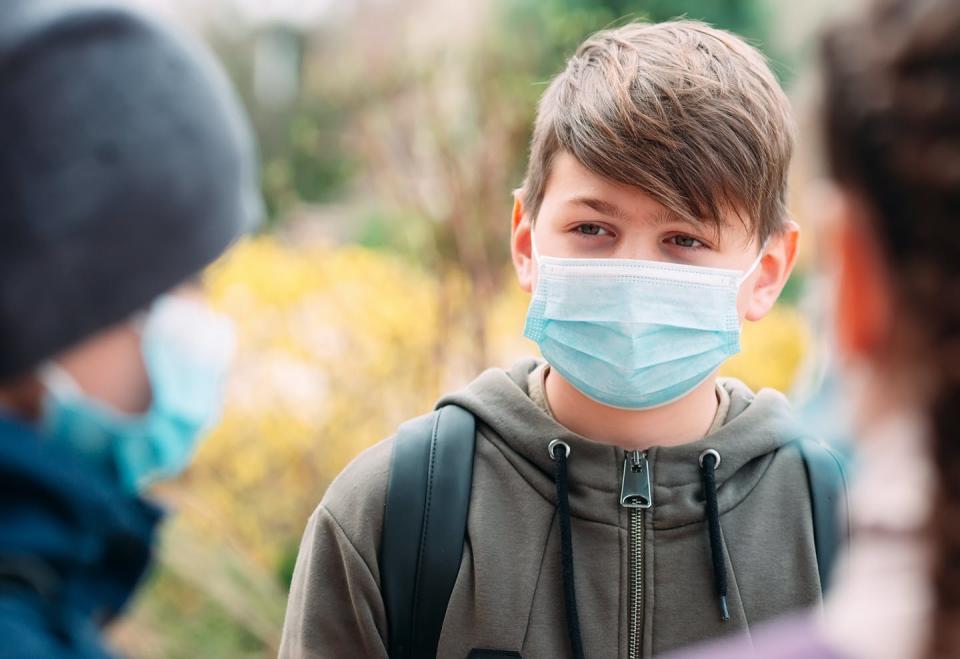 Masked boy stands outside school, talking to his friends.