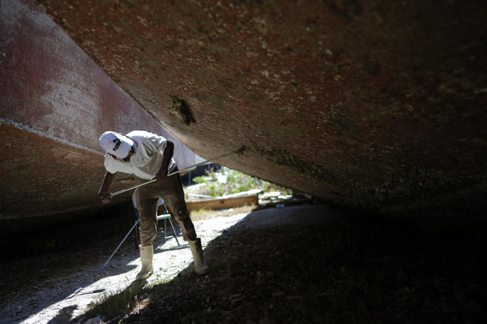 Michael Etwaru scrapes barnacles from the hull of a boat, as workers find a silver lining to the grounding caused by Hurricane Ian, on San Carlos Island in Fort Myers Beach, Fla., Friday, Oct. 7, 2022. (AP Photo/Rebecca Blackwell)