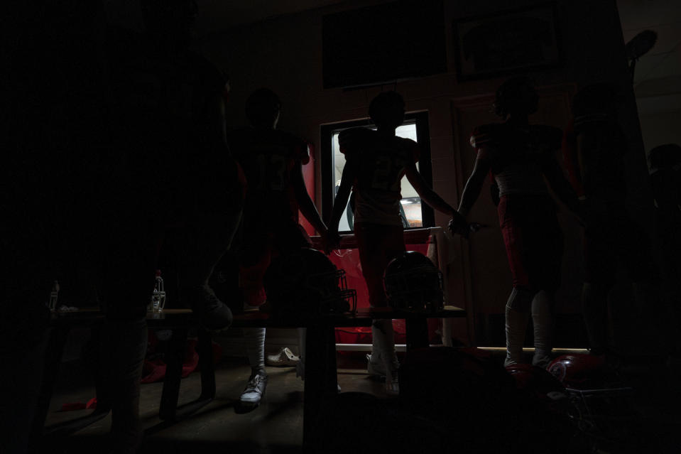 Lahainaluna High School football team members hold hands in a darkened locker room and sing the alma mater in Hawaiian after a game Saturday, Oct. 21, 2023, in Lahaina, Hawaii. Lahainaluna’s varsity and junior varsity football teams are getting back to normal since the devastating wildfire in August. (AP Photo/Mengshin Lin)