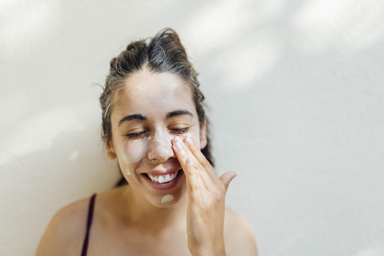 A close-up portrait of a young, happy hispanic woman applying sunscreen to her cheeks and forehead. The millennial accentuating her natural beauty. Her face is turned towards the camera, capturing the playful and carefree spirit of youth. The image conveys a sense of warmth, happiness, and contentment.