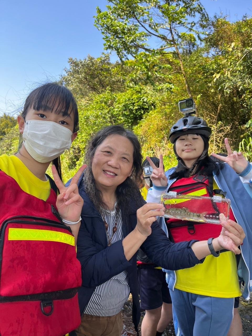 學生探索在地溪流，找到生物放在透明的盒子裡(窺箱)觀察，之後再放回溪流。中為劉松英校長。