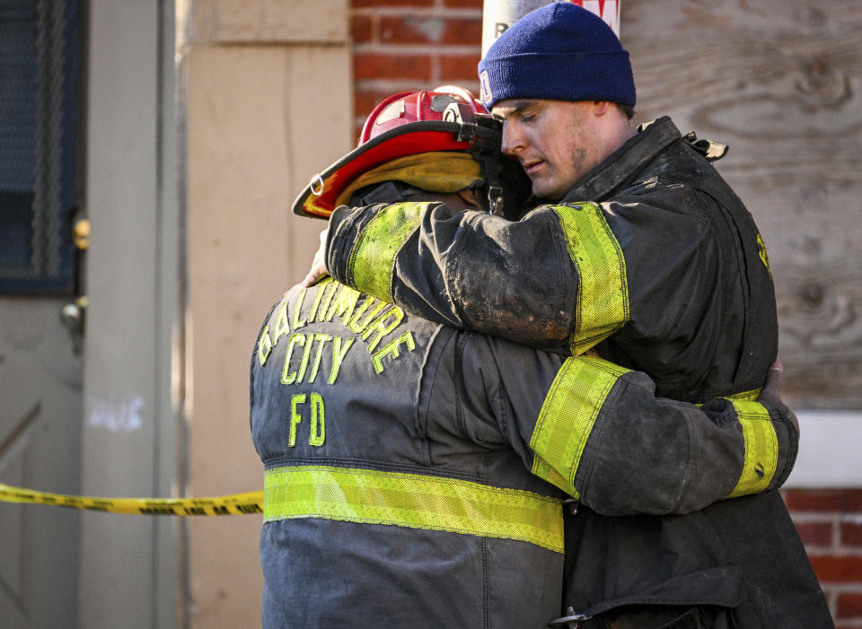 Baltimore City firefighters embrace at the scene of a vacant row house fire in Baltimore, Monday, Jan. 24, 2022. (Jerry Jackson/The Baltimore Sun via AP)