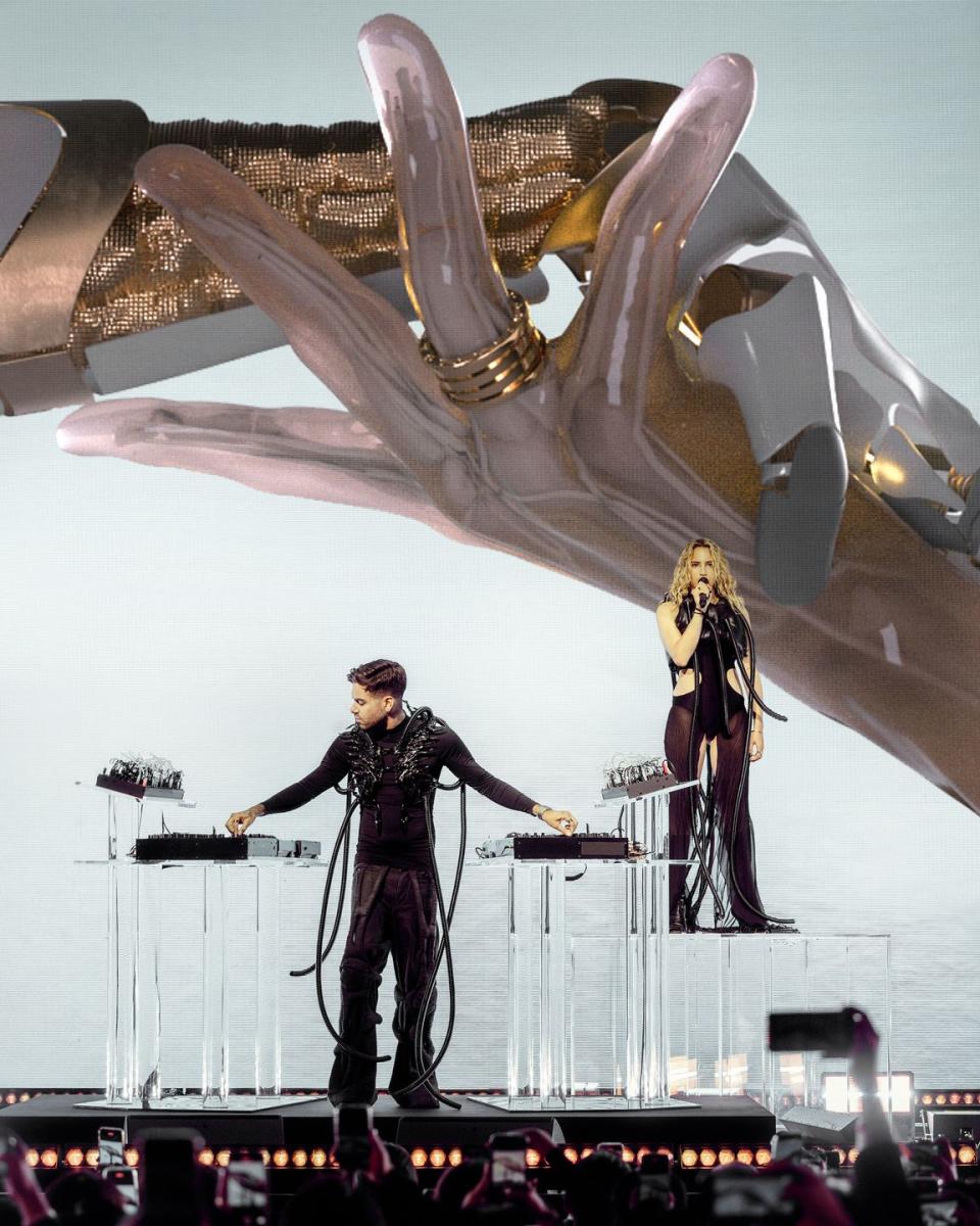 a man and woman on stage with an image of hands clasping at the back with an emphasis on the rings on the fingers