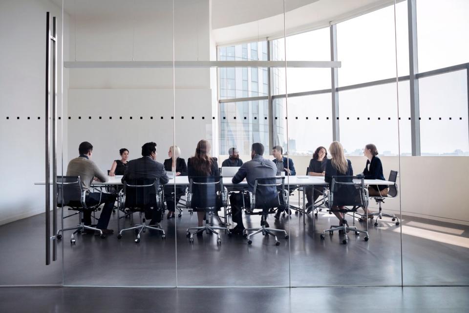 Professionally-dressed executives having a meeting around a table in a glass-walled conference room.