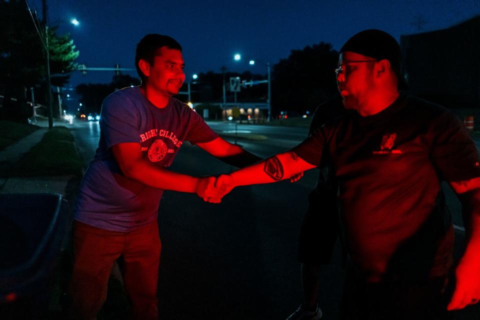 A smiling man, left, shakes hands with another man with a tattoo on his arm