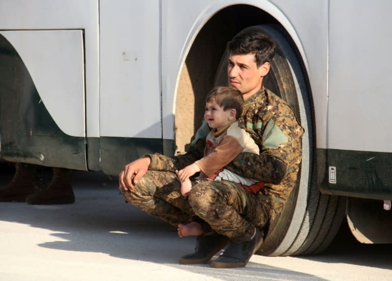 A Syrian pro-government fighter sits with a child as civilians and fighters from the government-held towns of Fuaa and Kafraya wait on April 19, 2017 at the rebel-held transit point of Rashidin