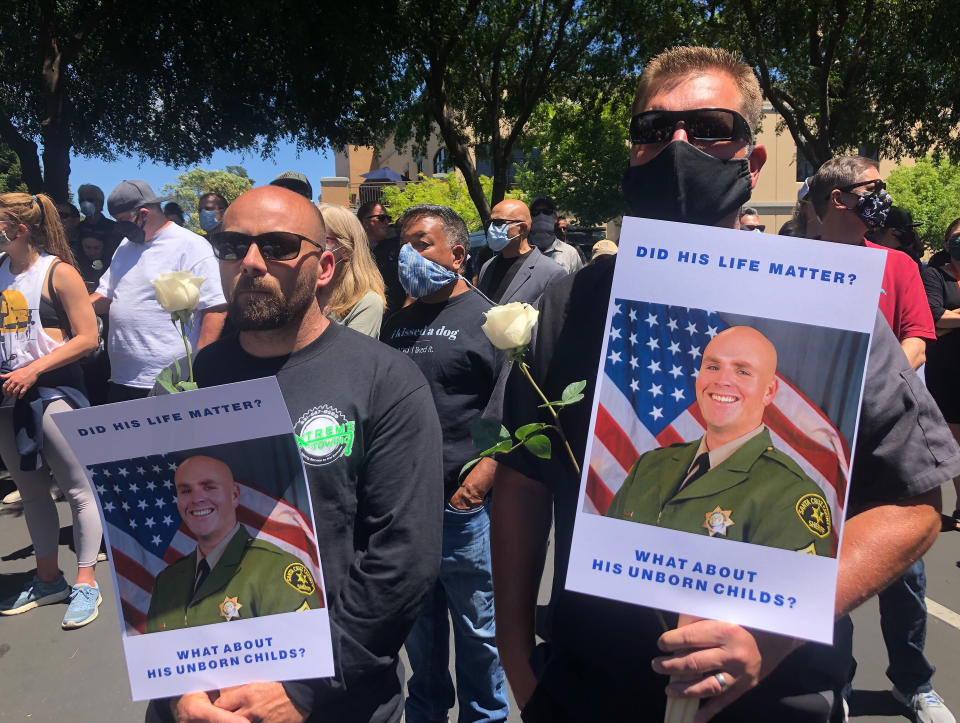 Matthew Rose, left, and Michael Carr, of Santa Cruz County hold posters of slain Sgt. Damon Gutzwiller, as they join others outside the Santa Cruz County Sheriff-Coroner's Office to pay their respects in Santa Cruz, Calif., Sunday, June 7, 2020. Santa Cruz County Sheriff's Sgt. Gutzwiller, 38, was shot and killed in Ben Lomond, an unincorporated area near Santa Cruz. Sheriff Jim Hart said the suspect, Steven Carrillo, was shot during the arrest and is being treated at a hospital. (AP Photo/Martha Mendoza)