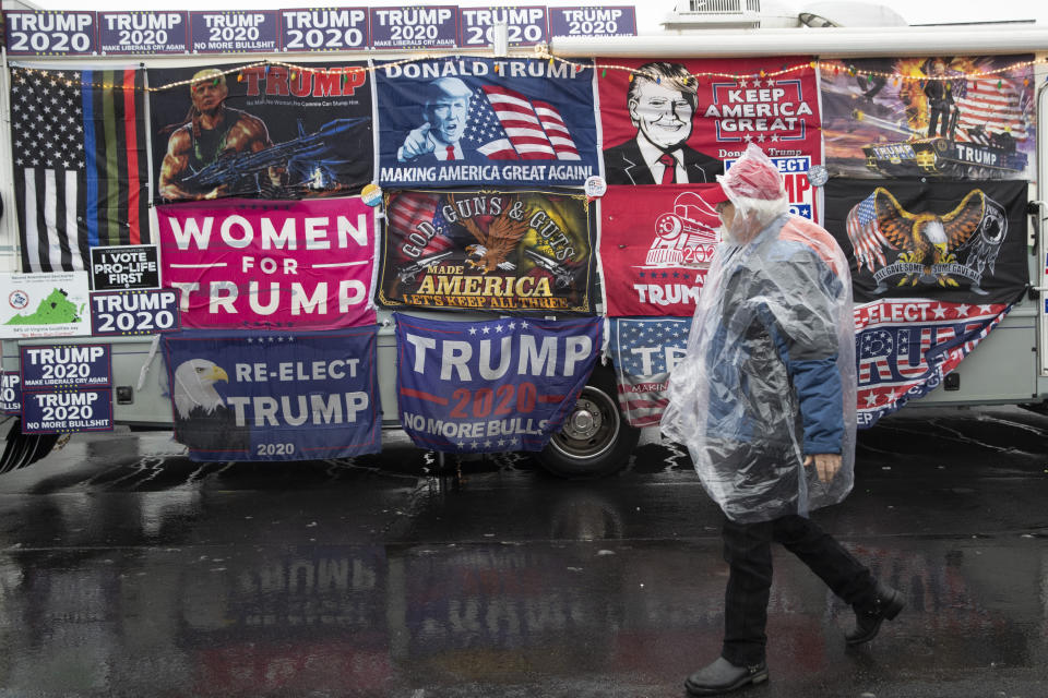 A man in a rain cover walks past a vehicle decorated with flags in support of President Donald Trump near the venue where the president will hold a campaign rally in the evening, Monday, Feb. 10, 2020, in Manchester, N.H. (AP Photo/Mary Altaffer)