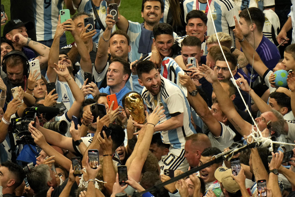 Argentina's Lionel Messi, center, holds the winners trophy as he celebrates with fans after Argentina won the World Cup final soccer match against France at the Lusail Stadium in Lusail, Qatar, Sunday, Dec. 18, 2022. (AP Photo/Francisco Seco)