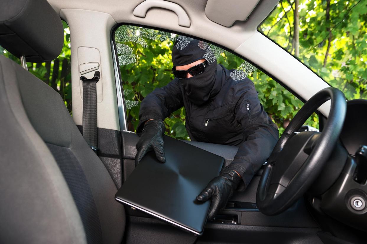 burglar stealing laptop from a car whose windows he broke forcefully