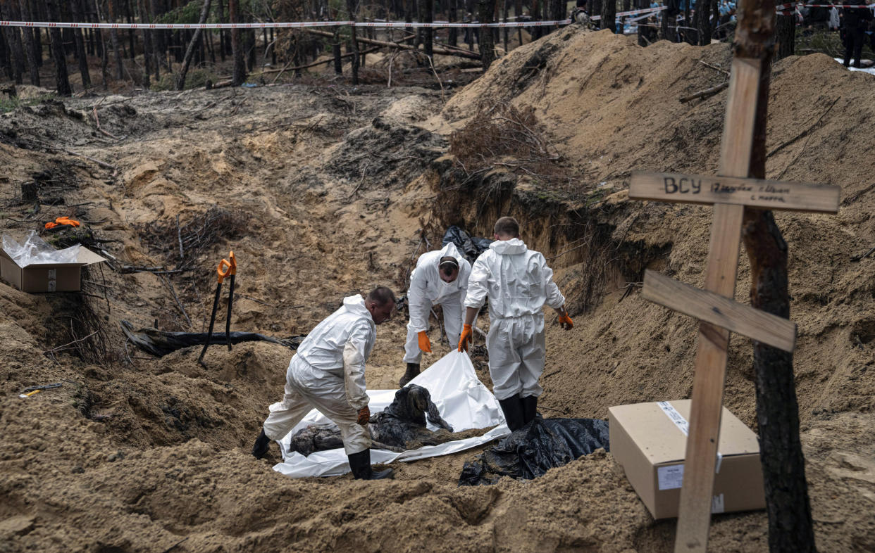 Experts work around a body during an exhumation in the recently retaken area of Izium, Ukraine, Friday, Sept. 16, 2022. Ukrainian authorities discovered a mass burial site near the recaptured city of Izium that contained hundreds of graves. It was not clear who was buried in many of the plots or how all of them died, though witnesses and a Ukrainian investigator said some were shot and others were killed by artillery fire, mines or airstrikes. (AP Photo/Evgeniy Maloletka)