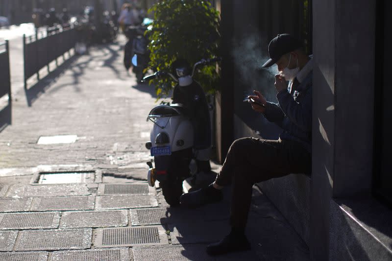 A man wearing a mask smokes on a street in Shanghai