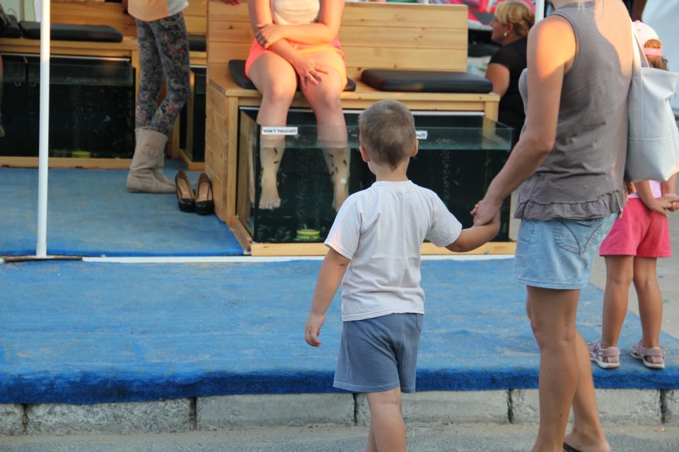 This Aug. 19, 2012 photo released by Mikhail Iliev shows people watching as a woman woman gets a fish pedicure in Sunny Beach, Bulgaria. A visit to Bulgaria can alternately feel like taking like a step back in time and witnessing a society that has modernized at warp speed. Mules and Ferraris share the freeways. Near a store selling Prada and Versace clothes, old women peddle handmade crocheted doilies and embroidered tablecloths. Dilapidated Soviet-style apartment buildings teem with people, as does a sparkling new shopping mall. (AP Photo/Mikhail Iliev)