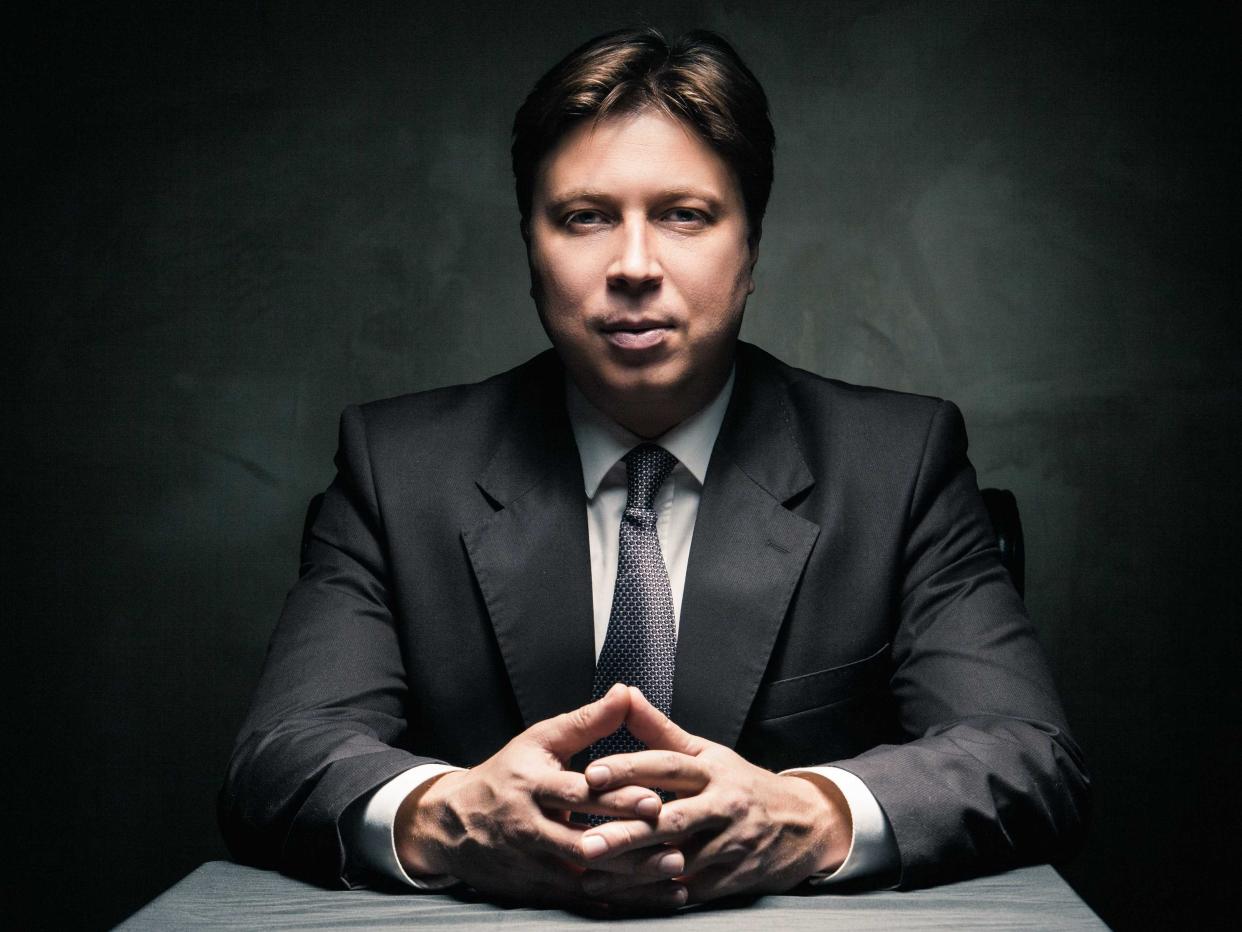 Man in suit sitting in dark room illuminated only by light from a lamp and looking in camera