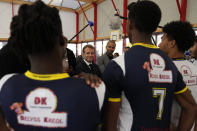 French President Emmanuel Macron, center, and former NBA player Tony Parker, behind, talk with members of a basketball team at a basketball playground in Tremblay-en-France, outside Paris, Thursday, Oct.14, 2021. French President Emmanuel Macron will promote sports ahead of the 2024 Olympic Games in Paris. (AP Photo/Francois Mori, Pool)