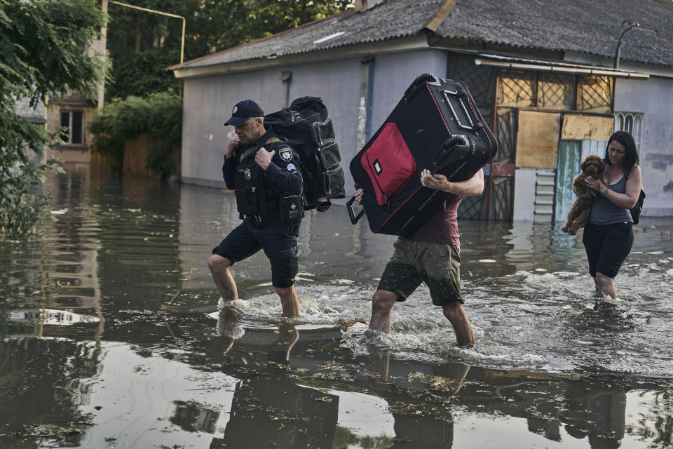 Local residents carry their belongs as they evacuated from a flooded neighborhood in Kherson, Ukraine, Tuesday, June 6, 2023. The wall of a major dam in a part of southern Ukraine has collapsed, triggering floods, endangering Europe's largest nuclear power plant and threatening drinking water supplies. (AP Photo/Libkos)