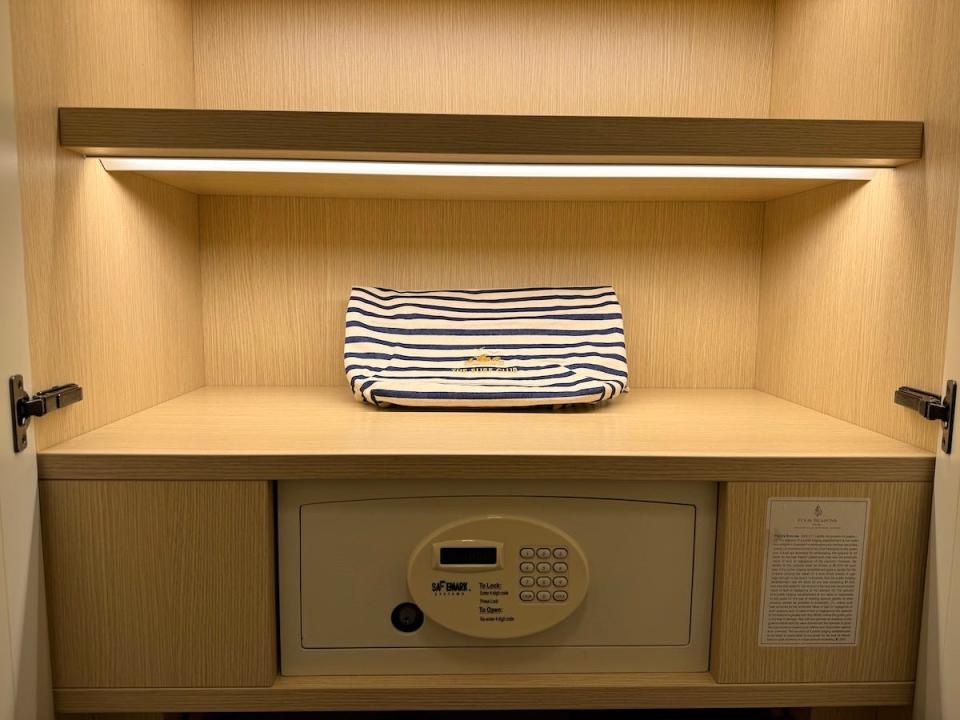 A blue-and-white striped tote bag with The Surf Club branding on a shelf on the inside of a hotel closet above a safe.