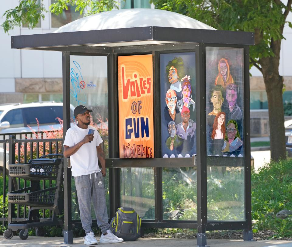 A man waits for a bus near a new bus stop mural at North 12th Street and West State Street carrying a message that Milwaukee has a gun violence problem that needs to be stopped in Milwaukee on Thursday, June 23, 2022.