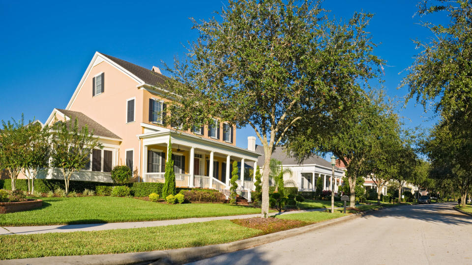 Picturesque luxury home with wooden verandah in traditional style overlooking quiet suburban streets under clear blue panoramic skies in this tranquil Florida community.