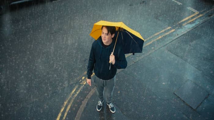 A boy stands in rain with an umbrella over his head