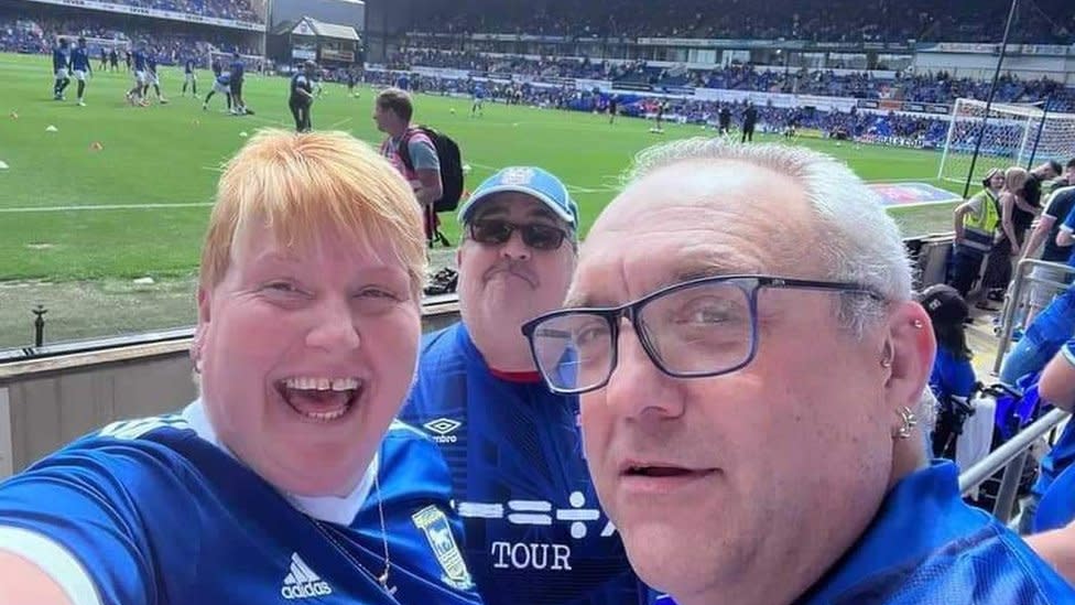 Nina and Gary Battle, alongside Steve Kirby pitch side at Portman Road, all wearing their Ipswich Town replica kits.