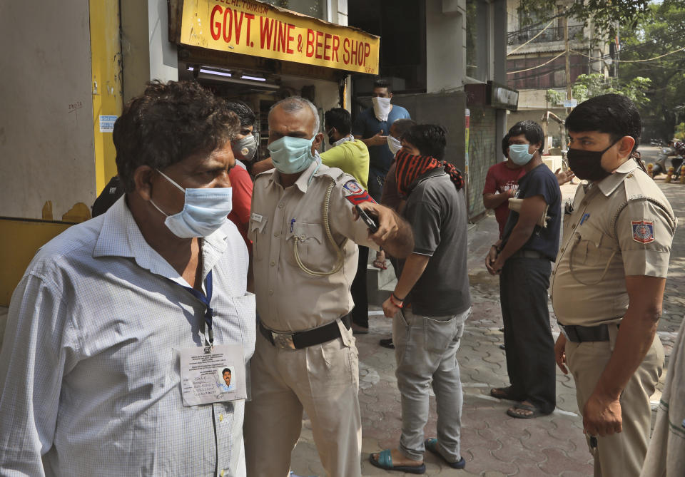 A policeman asks a man to stand in the queue as people line up outside one the liquor shops which was reopened Monday after six weeks lockdown in New Delhi, India, Monday, May 4, 2020. India's six-week coronavirus lockdown, which was supposed to end on Monday, has been extended for another two weeks, with a few relaxations. Locking down the country's 1.3 billion people has slowed down the spread of the virus, but has come at the enormous cost of upending lives and millions of lost jobs. (AP Photo/Manish Swarup)