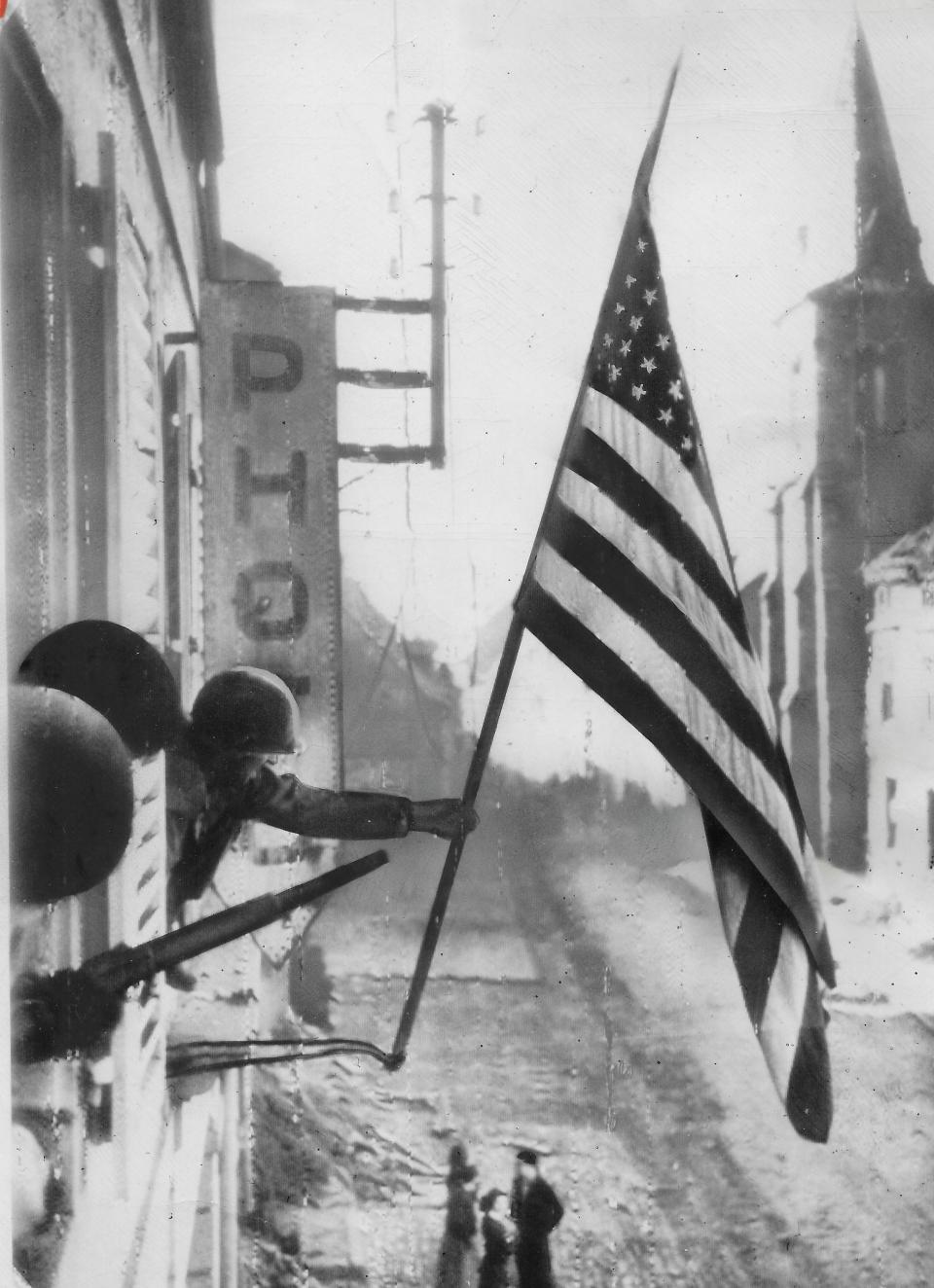 U.S. Army Capt. Thomas H. Garahan of Brooklyn, New York, hangs an American flag from a window after troops liberated a French village from German occupation in March 1945.