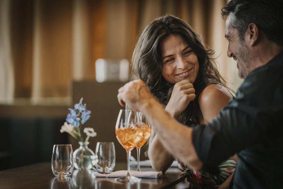 A man and a woman share a laugh and drinks at a cozy restaurant table with flowers