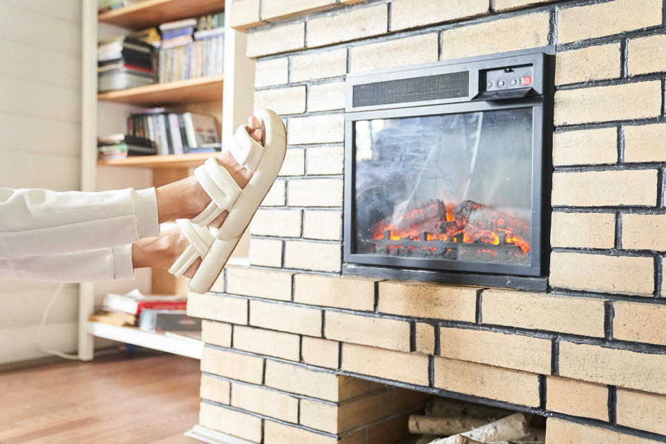 Person warming their feet by an electric fireplace with sandals on