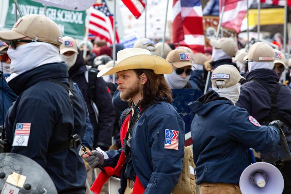 Un hombre con barba y cabello castaño largo con un sombrero de vaquero rodeado de miembros del Frente Patriota