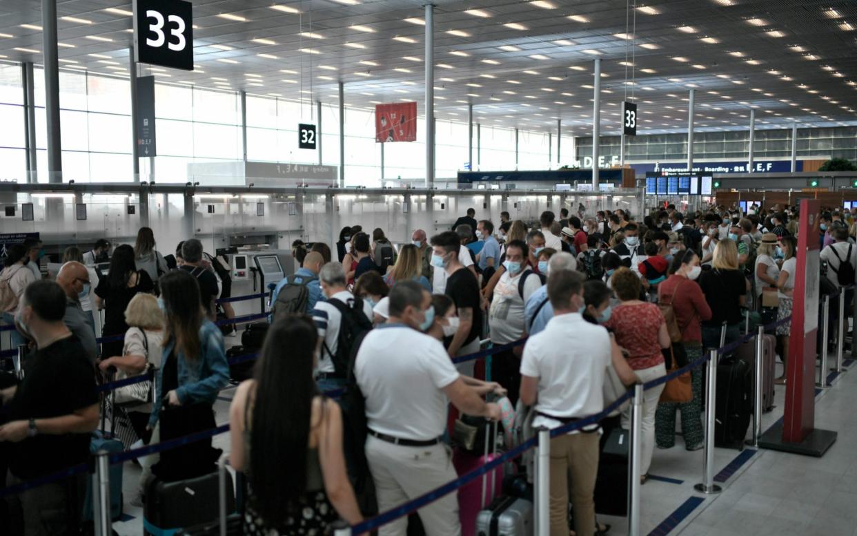 Travelelrs, wearing protective face masks, line up at a check-in desk of the Orly Airport, south of Paris on August 1, 2020 during a major weekend of the French summer holidays - Stephanie de Sakutin/AFP