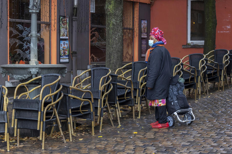 FILE - A woman wears a face mask to protect herself against the coronavirus as she passes by an empty terrace in the Marrolles quarter in Brussels, Belgium, Nov. 17, 2021. As countries across Europe reimpose lockdowns in response to surging COVID-19 cases and deaths, the UK – long one of Europe’s hardest-hit countries -- carries on with a policy of keeping everything as normal as possible. (AP Photo/Olivier Matthys, File)