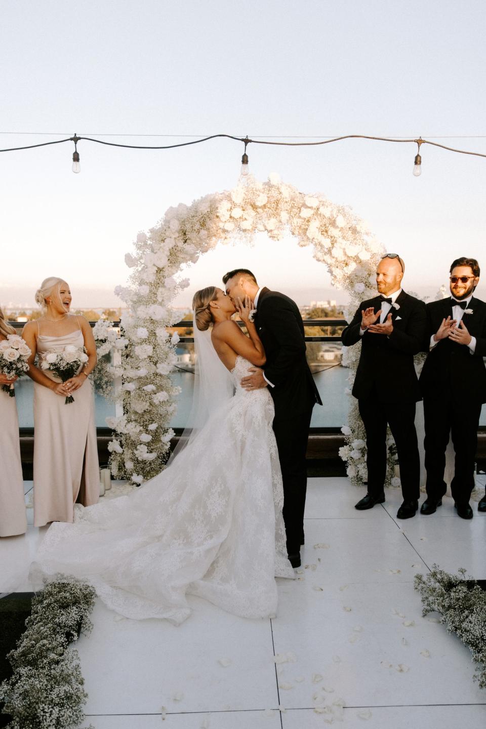 A bride and groom kiss in front of a floral arch during their wedding ceremony.