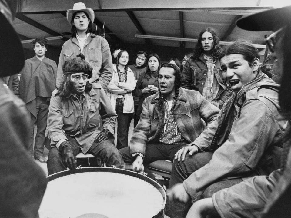 Members of the American Indian Movement (AIM) chant and beat a drum to serenade those who will man the outposts during the Wounded Knee Occupation
