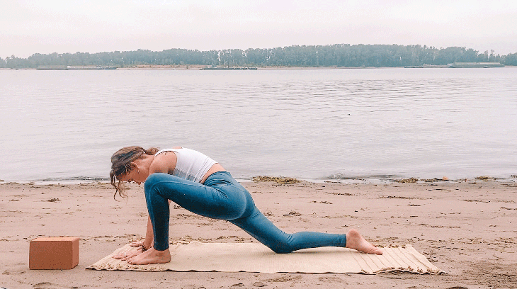 Woman in a low lunge on her yoga mat at the beach during the full Moon in Pisces