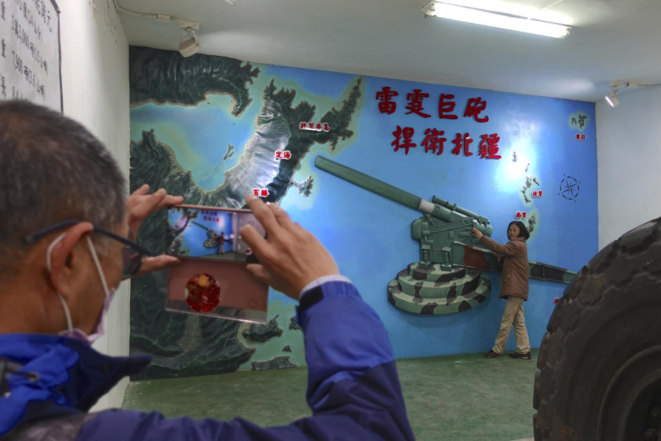 A tourist pose for photos near a mural depicting a howitzer pointing towards mainland China's Fujian province at a base museum in Nangan, part of Matsu Islands on Monday, March 6, 2023. Just 10km away from mainland China at its closest, Matsu became a fortress and frontline of defense for the Nationalists who had retreated to Taiwan in 1949 after losing to the Communist Party in a civil war. (AP Photo/Johnson Lai)