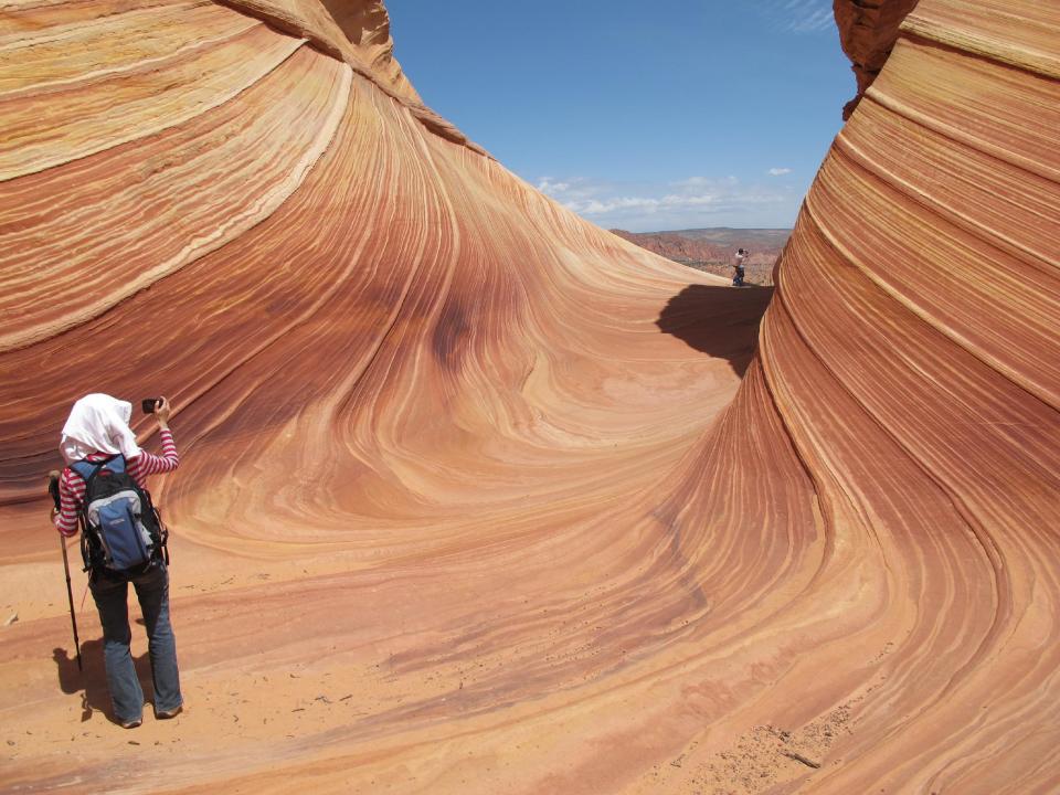 This May 28, 2013 photo shows a hiker taking a photo on a rock formation known as The Wave in the Vermilion Cliffs National Monument in Arizona. The U.S. Bureau of Land Management limits the number of permits for hikers to 20 a day in order to preserve the backcountry wilderness experience and protect the sandstone formation. (AP Photo/Brian Witte)