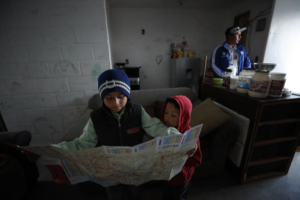 In this July 10, 2019, photo, Nahum Perla, left, studies a San Diego map with his younger brother, Carlos Isai Perla, as their father, Juan Carlos Perla, right, gets ready to make the journey from their home on the outskirts of Tijuana, Mexico, to San Diego for an asylum hearing. The Perlas are faring better than most of the roughly 60,000 asylum-seekers returned to Mexico under a Trump administration policy, many of whom live in fear of being robbed, assaulted, raped or killed. (AP Photo/Gregory Bull)