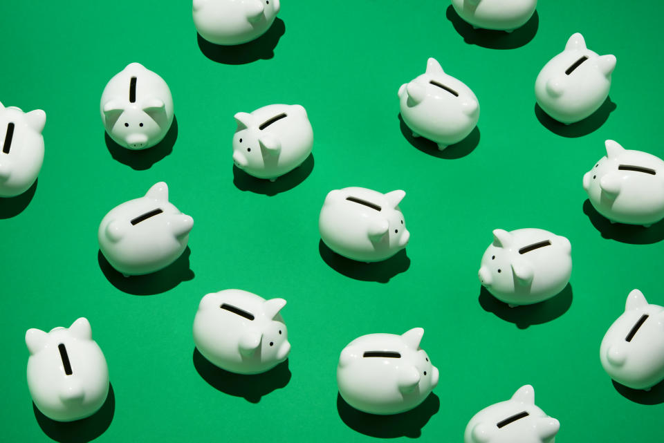 16 small white piggy banks placed randomly on green surface, high angle of view