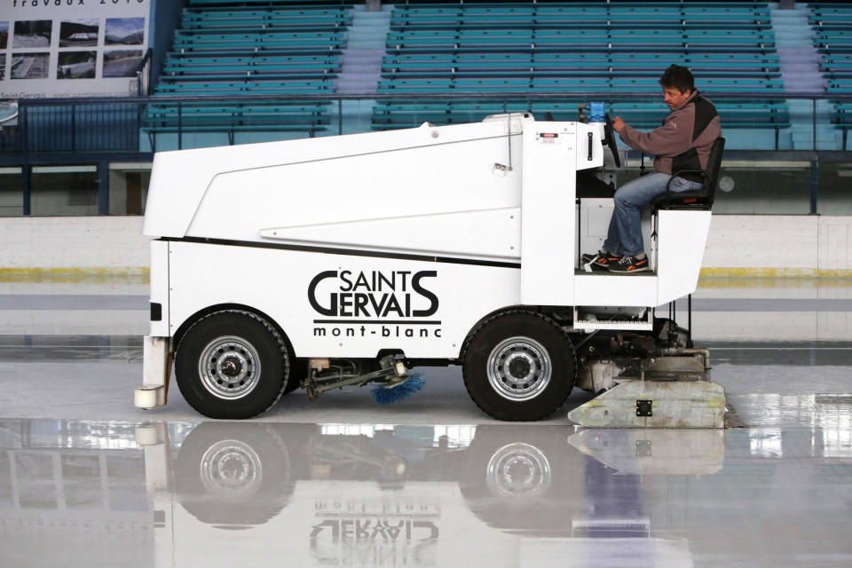 A person operates an ice resurfacing machine at an indoor ice rink. The machine has the text "Saint Gervais Mont-Blanc" on its side